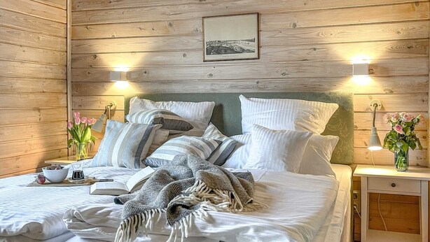 A cozy bedroom with a wooden wall, a bed with white bedding and striped pillows, a bedside table with a lamp, and a picture on the wall. - traumHaff®Romance of the boatswains with fireplace, private NORDICSPA, fireplace (Rieth am See)