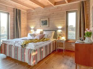 A wooden-paneled bedroom with a bed, bedside lamps, a nightstand, and a window with curtains.