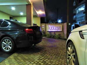 Una entrada con portón y un letrero que dice 'Vivas Residencies', con dos coches estacionados al frente.