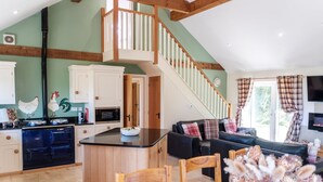 A spacious kitchen with wooden cabinets, a black stove, and a central island. A staircase leads to an upper level.
