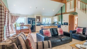 A spacious living area with a high ceiling, wooden beams, a dining table, sofas, and a kitchen in the background.