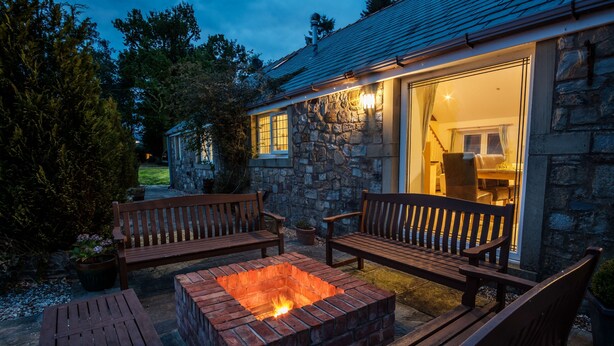 A stone building with a fire pit and wooden furniture.