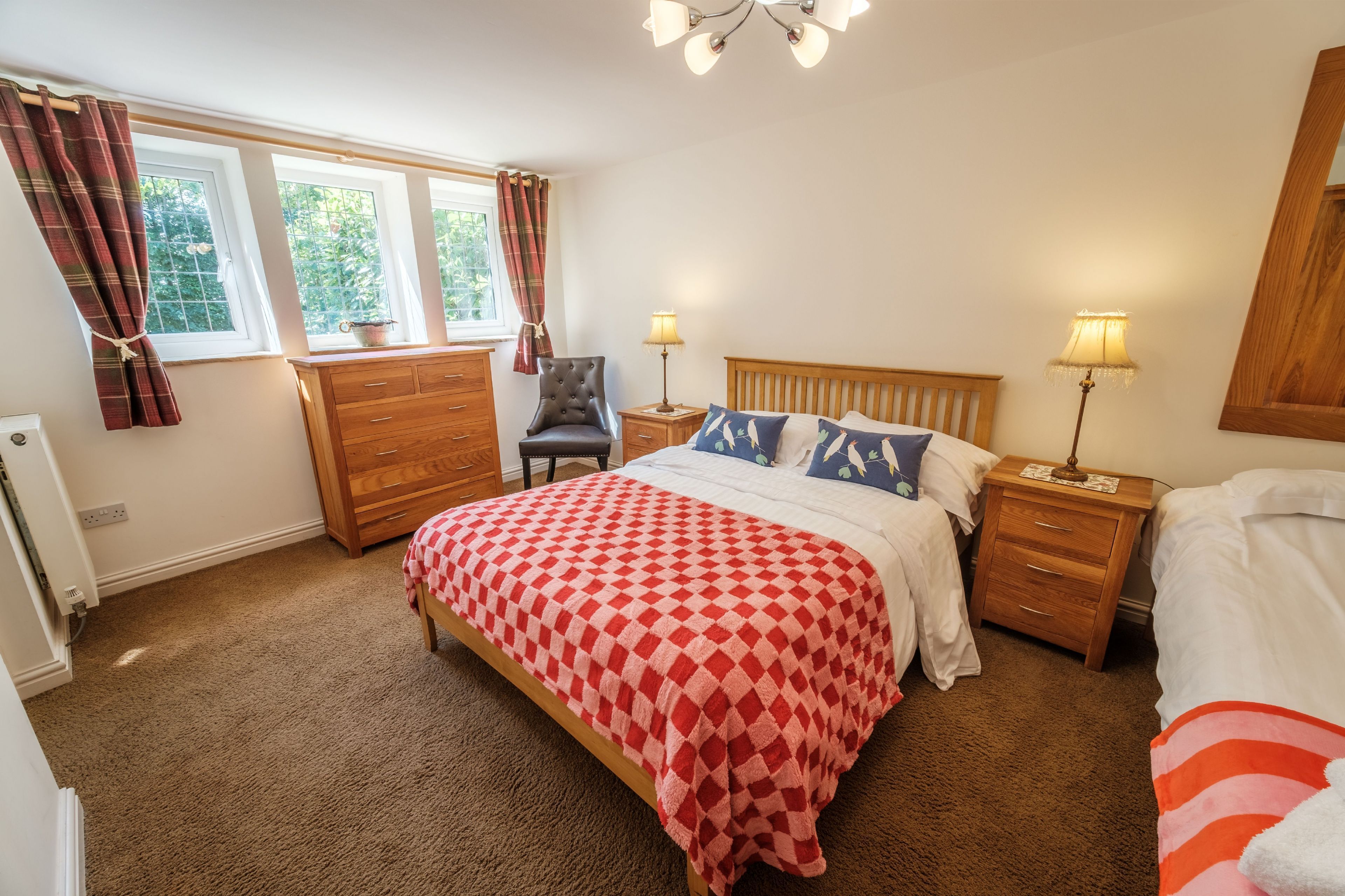 A bedroom with a bed, two bedside tables, a chair, a dresser, and a window with curtains.
