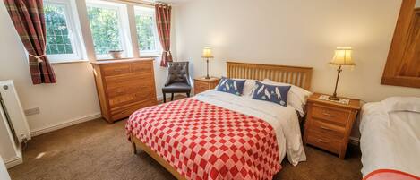 A bedroom with a bed, two bedside tables, a chair, a dresser, and a window with curtains.