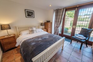 Une chambre à coucher avec un lit, une table de chevet, une chaise et une fenêtre avec des rideaux.