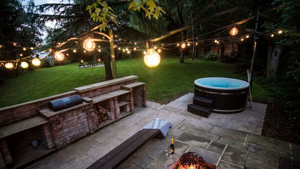 Eine Terrasse im Freien mit Steinboden, einem Feuerkorb, einem Whirlpool und Lichterketten.