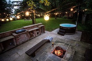 Une terrasse extérieure avec un sol en pierre, un foyer, un jacuzzi et des guirlandes lumineuses.