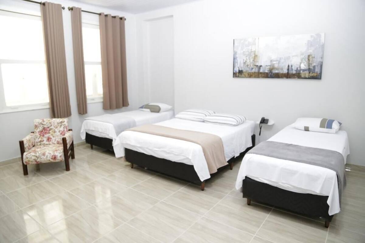 Ein Hotelzimmer mit drei Betten, einem Sessel und einem Gemälde an der Wand.