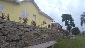 A yellow building with a stone wall and a wooden bench. - Hotel Pousada Cassino (Caete)
