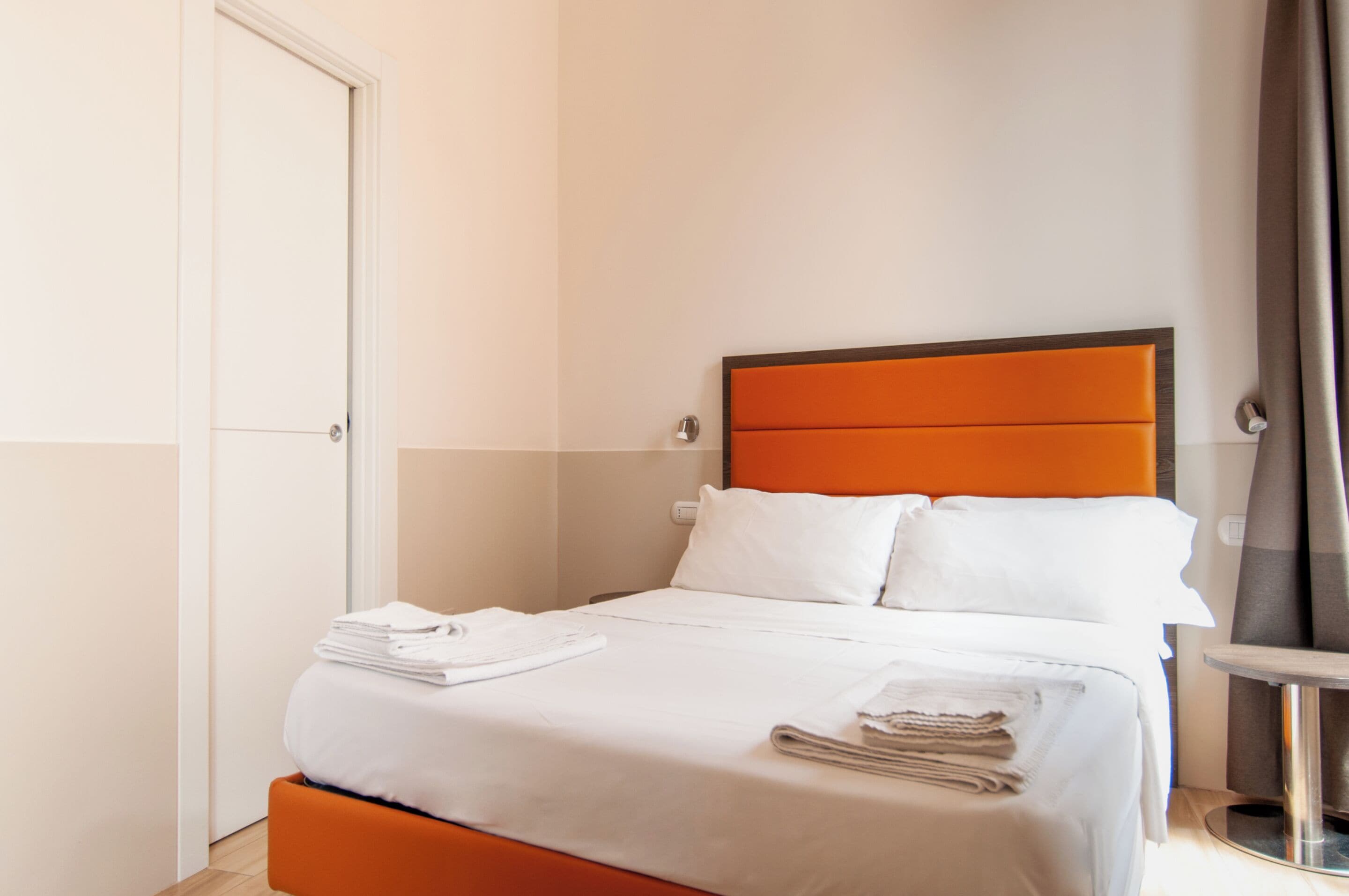 A hotel room with a bed, a bedside table, and a door.