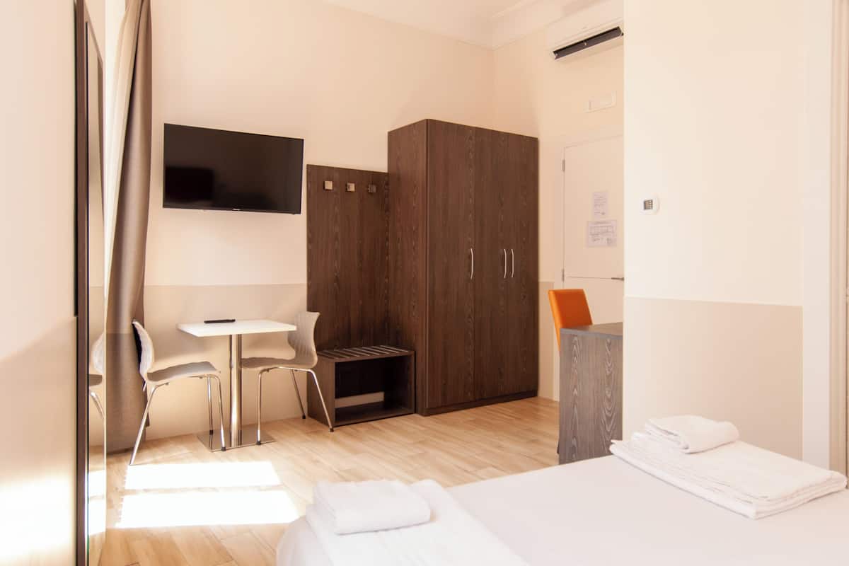 A hotel room with a bed, a desk, a chair, a wardrobe, and a TV on the wall.