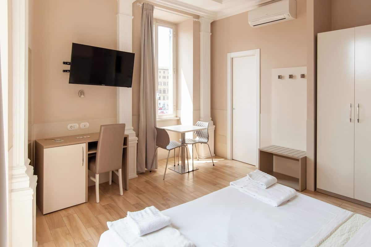 A hotel room with a bed, a desk, a chair, a TV, and a wardrobe.