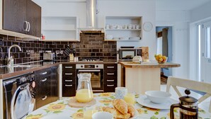 Eine moderne Küche mit Einbauofen, Mikrowelle und Geschirrspüler. Ein Frühstückstisch mit Croissants, Saft und Kaffeekanne.