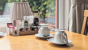 A breakfast table with a lamp, tea set, and condiments. - Sunnycroft Guesthouse (Llandudno)