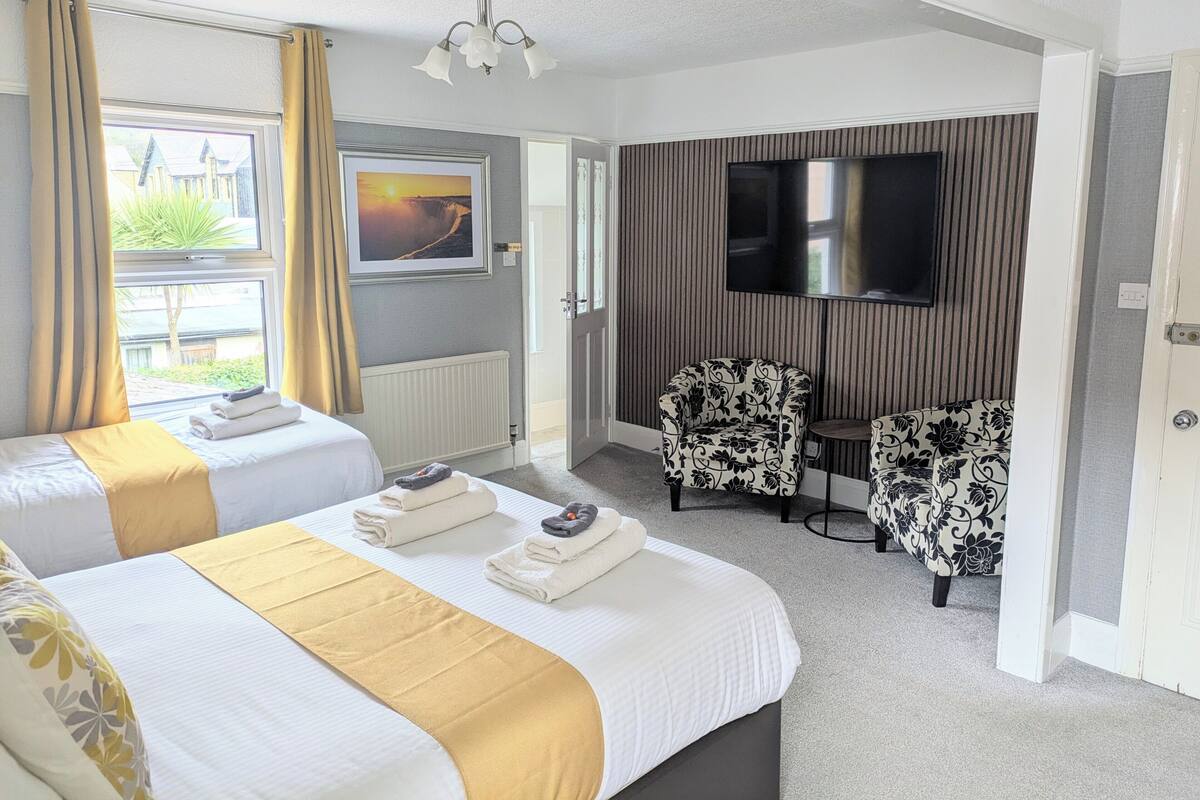 A hotel room with two beds, a TV, a window with curtains, and a view of the outside.