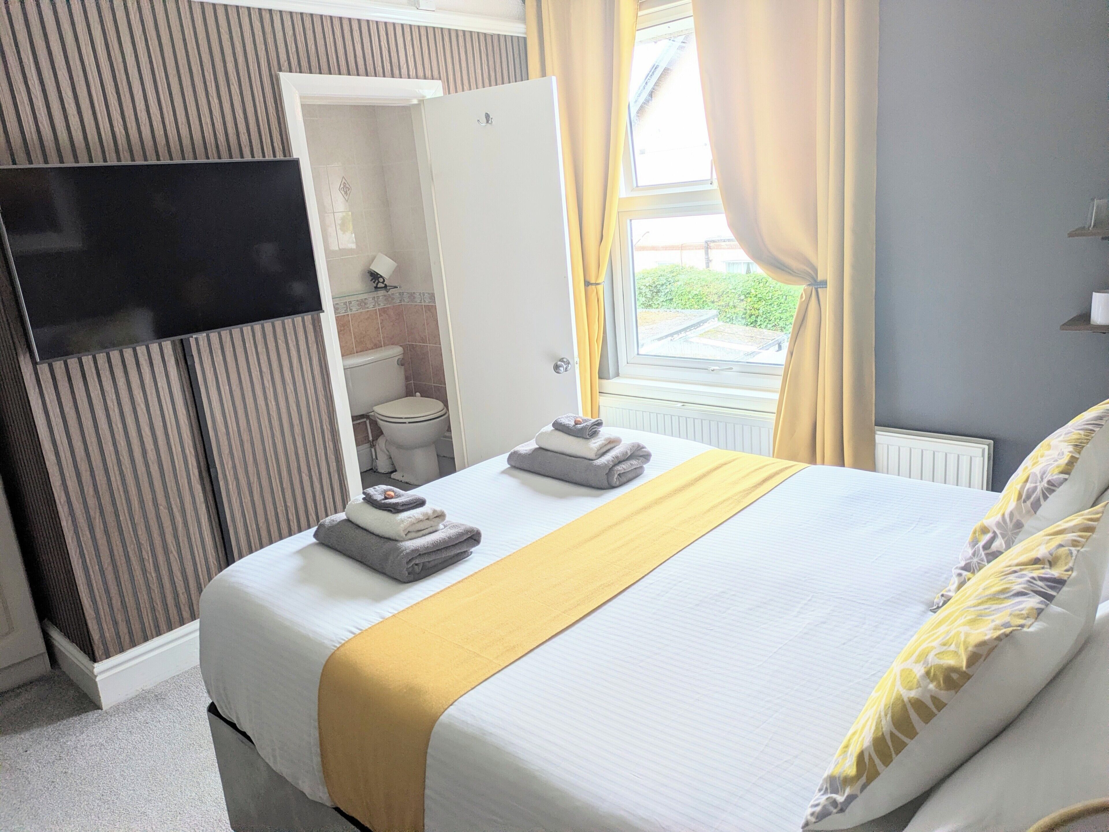 Een hotelkamer met een bed, een televisie, een badkamer zichtbaar door een geopende deur, en een raam met gordijnen.