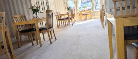 A spacious room with a carpeted floor, wooden furniture, and large windows with curtains.