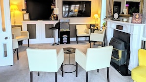 A living room with a fireplace, a television, a chandelier, and a bar area. - Sunnycroft Guesthouse (Llandudno)