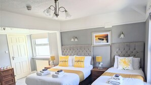 A hotel room with two beds, a large window, a framed picture on the wall, and a ceiling light. - Sunnycroft Guesthouse (Llandudno)