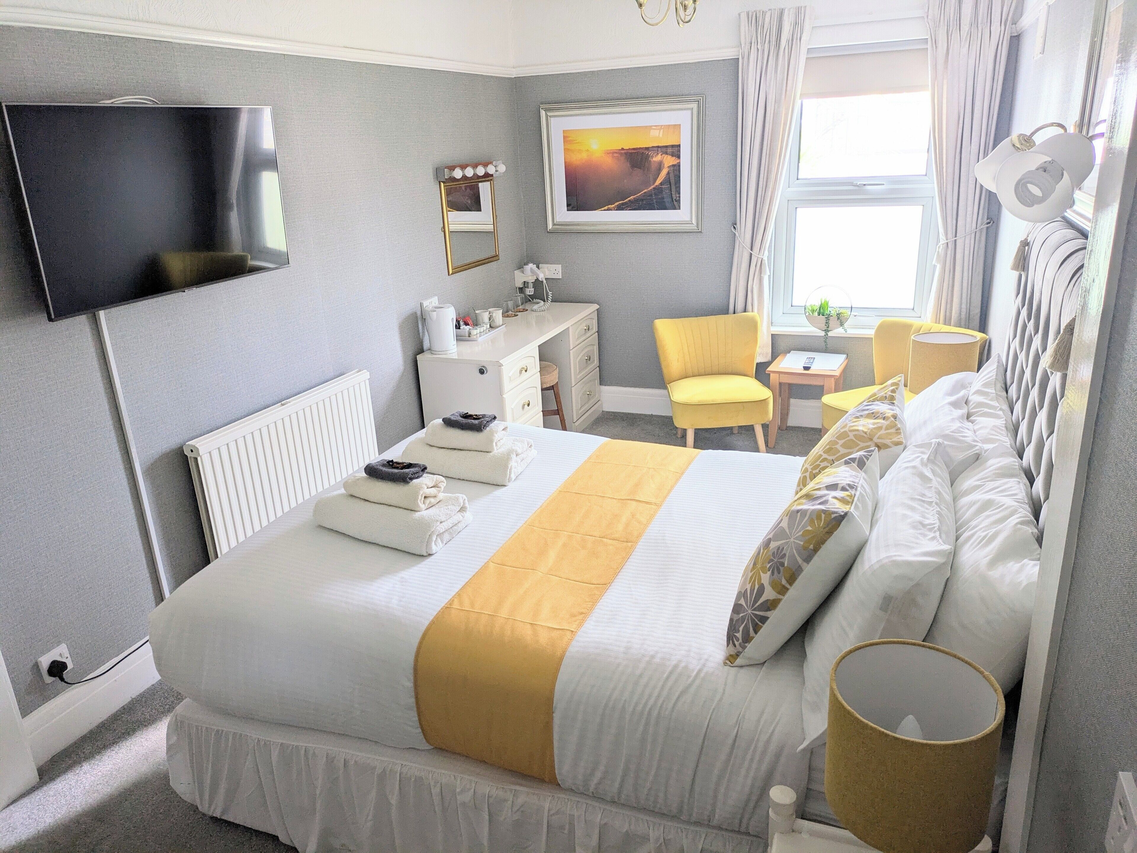 A hotel room with a bed, a desk, a chair, a TV, and a window with curtains.