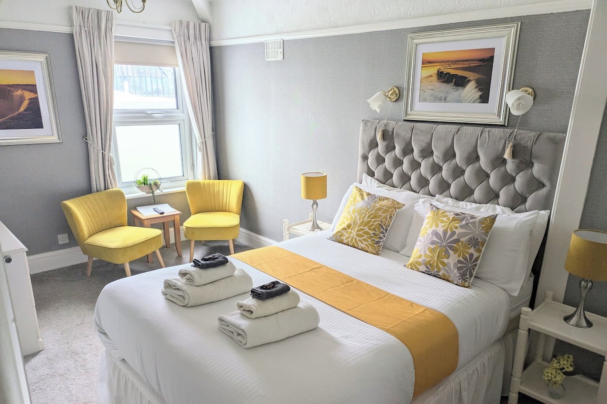 A neatly arranged hotel room with a large bed, two chairs, a desk, and a window with curtains.