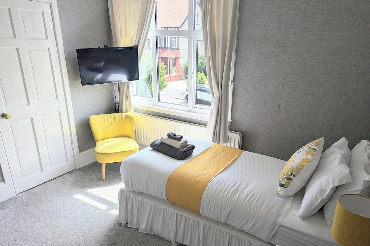 A hotel room with a bed, a chair, a TV, and a window with curtains.