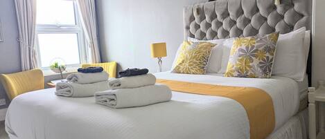 Una cama bien hecha con cabecera capitonada, una mesita de noche con lámpara y un cuadro en la pared.