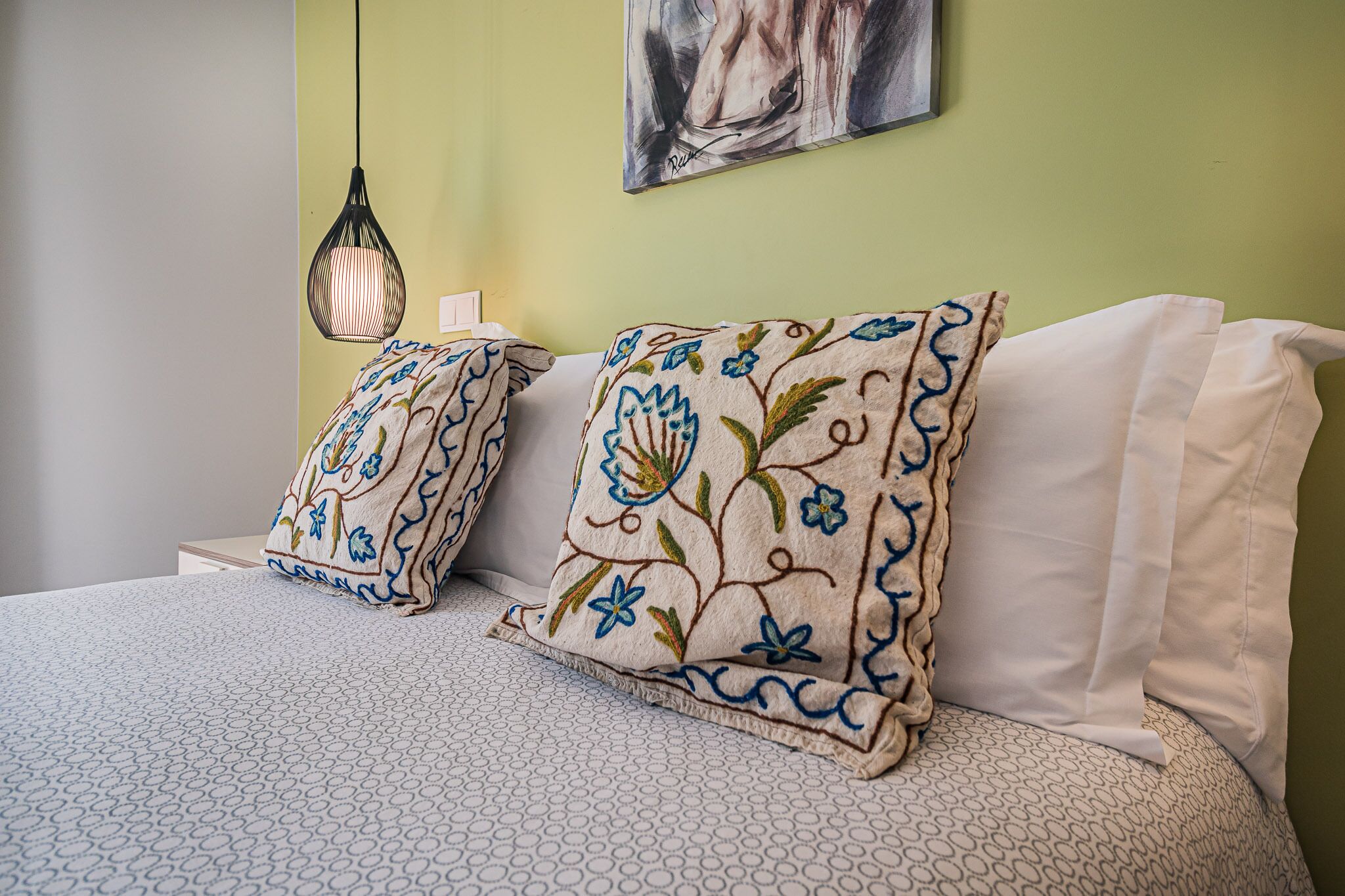 A bed with patterned pillows and a hanging light fixture.