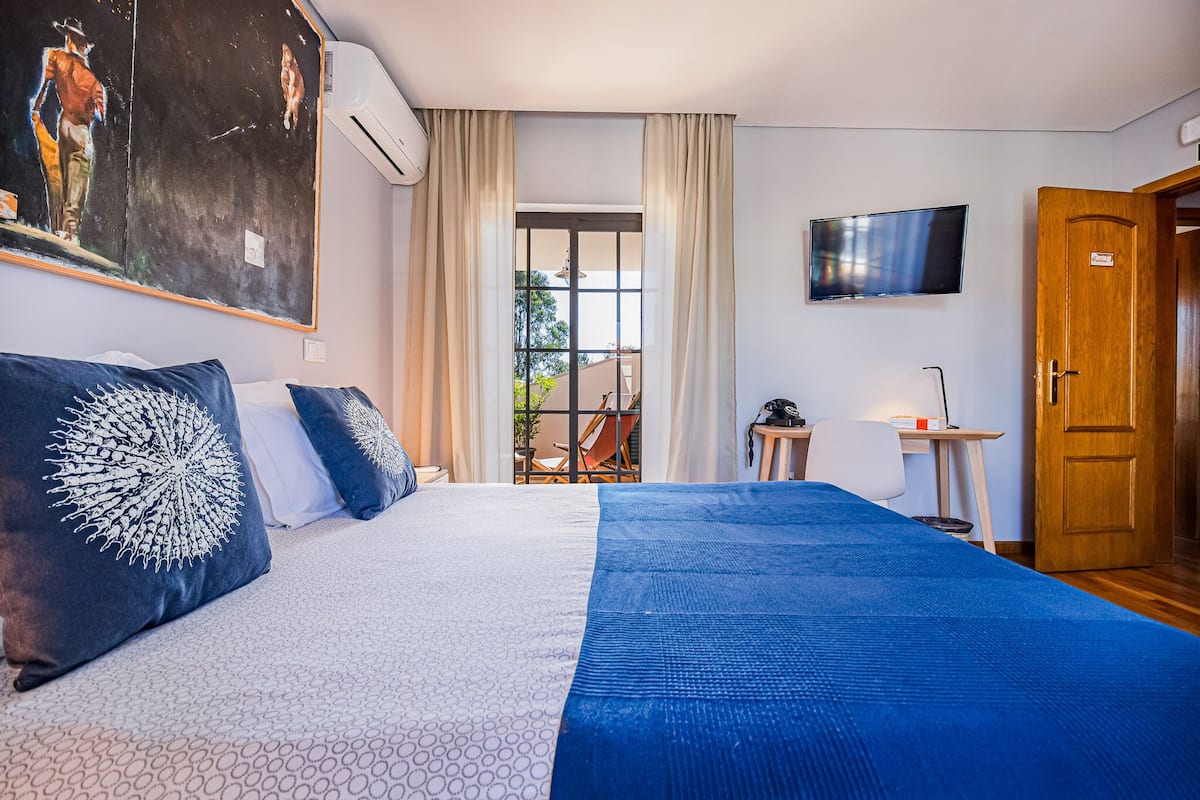 Een hotelkamer met een groot bed, een aan de muur bevestigde televisie, een bureau met een stoel en een deur.