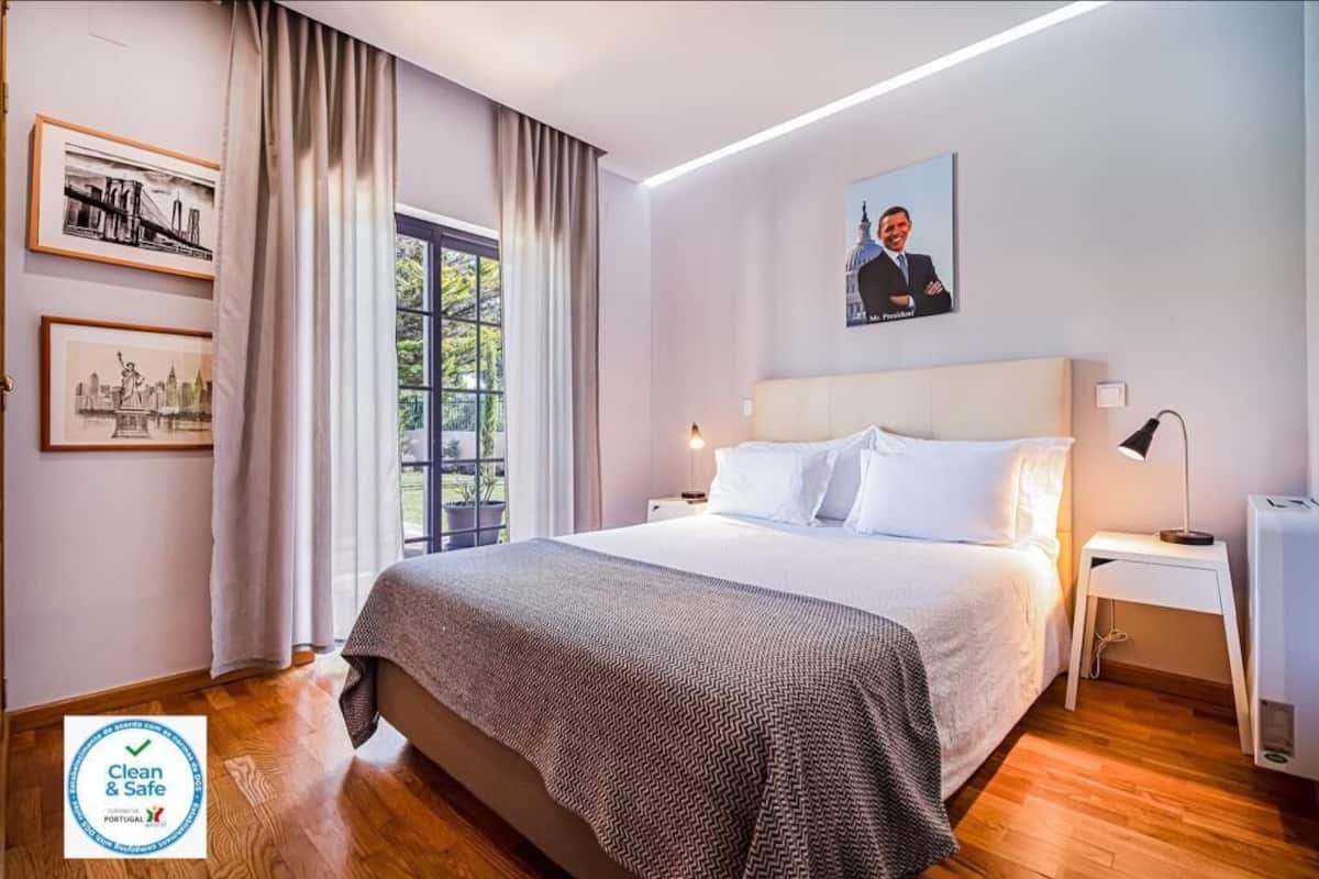 Een schone en veilige hotelkamer met een groot bed, een nachtkastje, een lamp en ingelijste foto’s aan de muur.