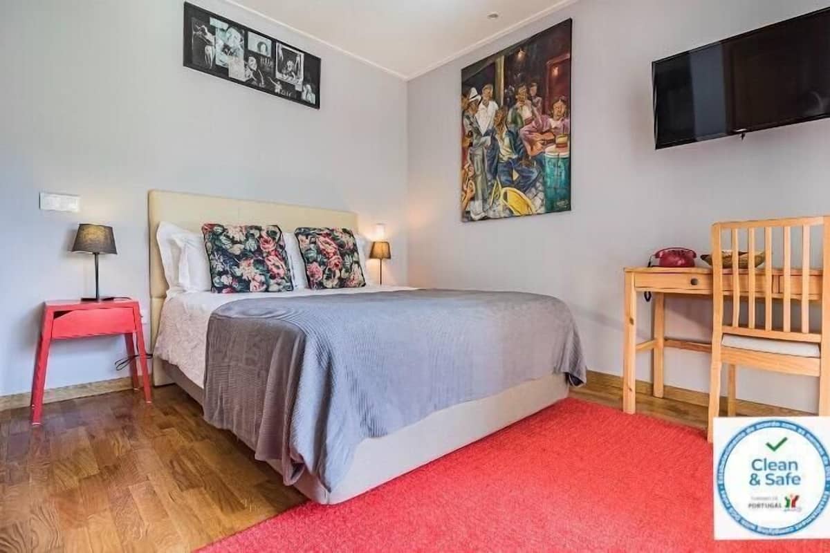 Een slaapkamer met een bed, een bureau, een stoel, een televisie en kunst aan de muren.