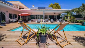 A poolside area with a wooden deck, two lounge chairs, a hammock, and a potted plant. - Buganvilia do Meco B&B (Sesimbra)