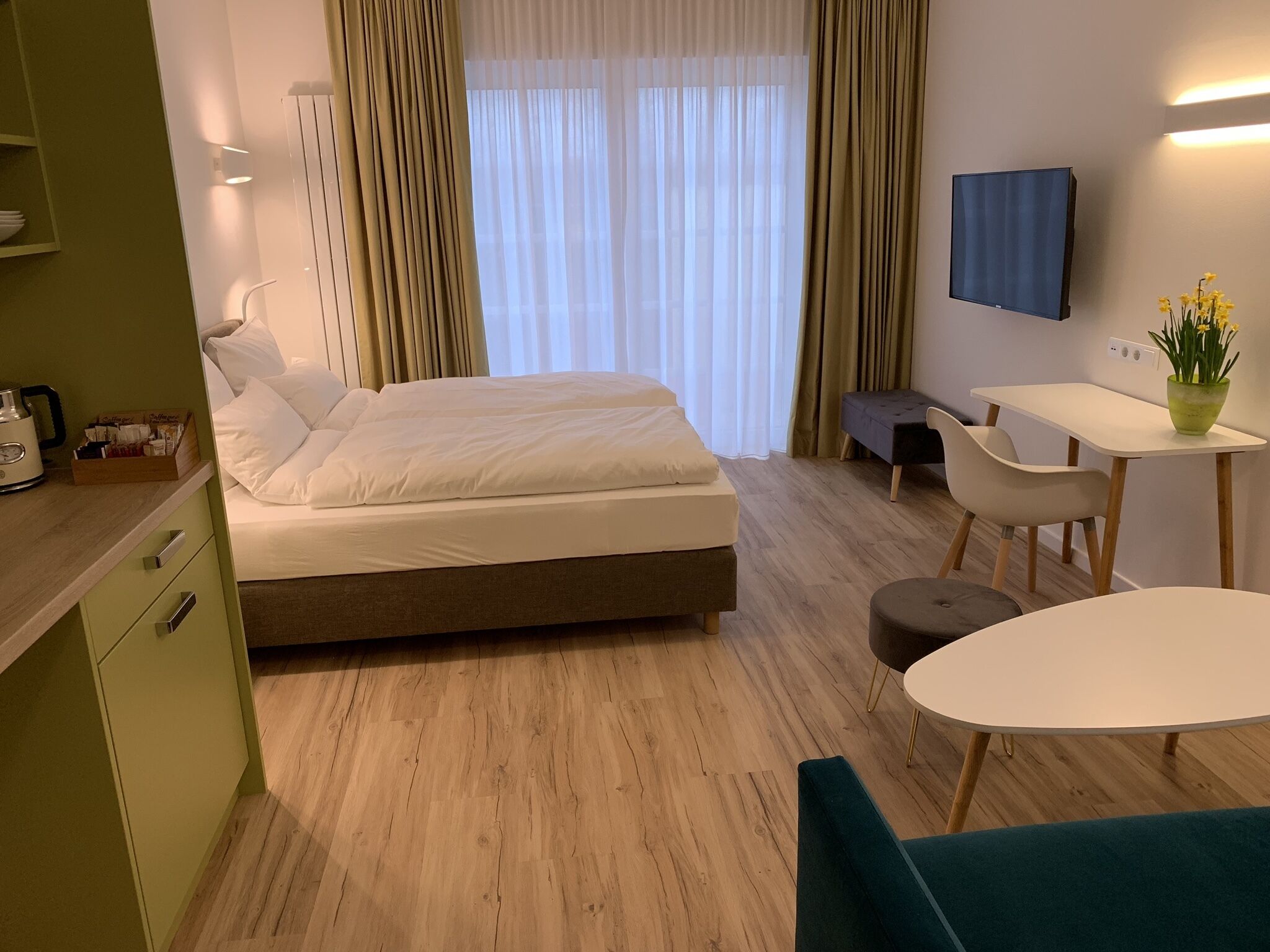 Una habitación de hotel con cama, escritorio, silla, televisión y una pequeña mesa con una planta.