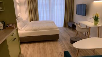Una habitación de hotel con cama, escritorio, silla, televisión y una pequeña mesa con una planta.