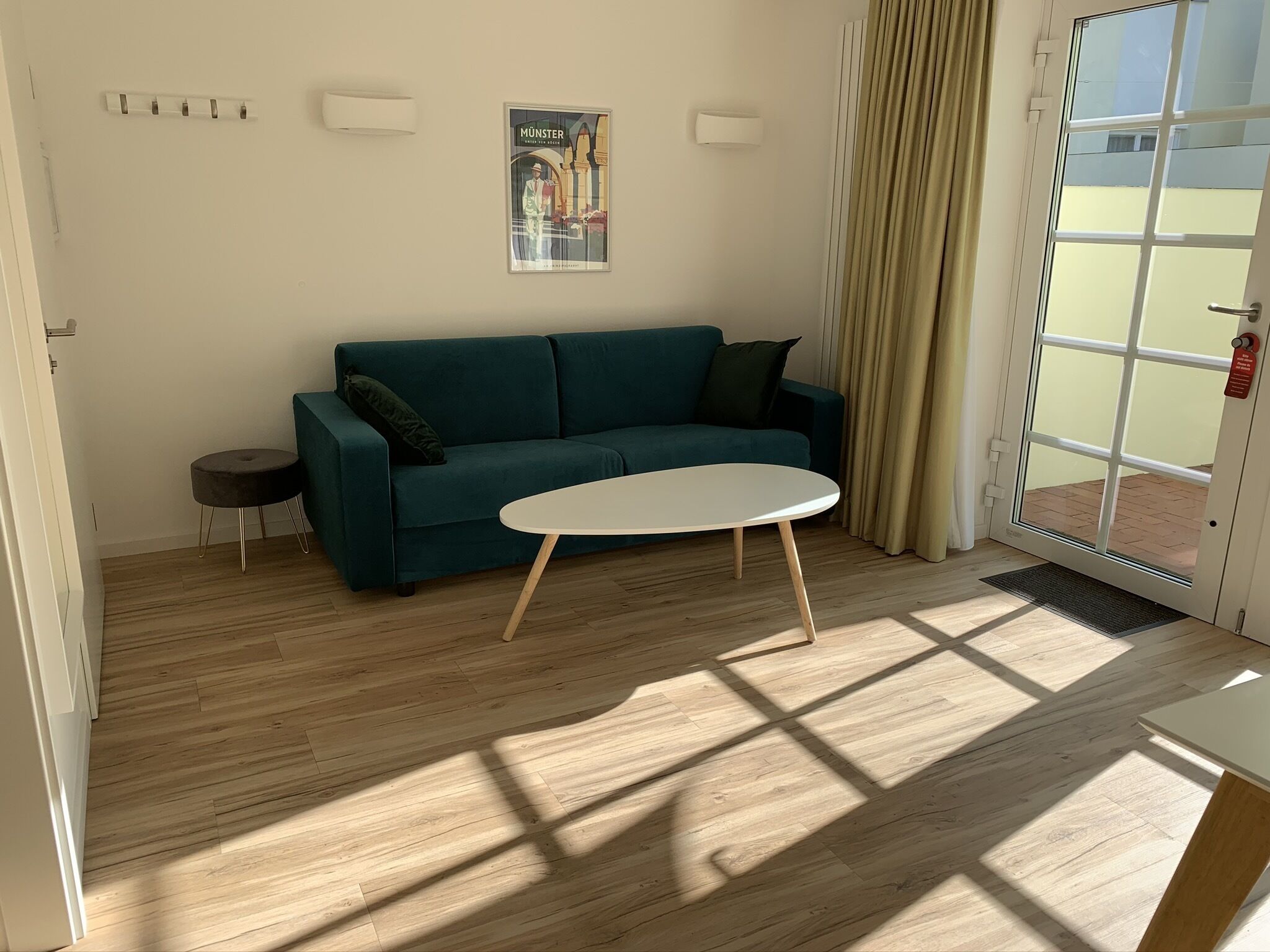 A room with a teal sofa, a round white table, and a door leading outside.