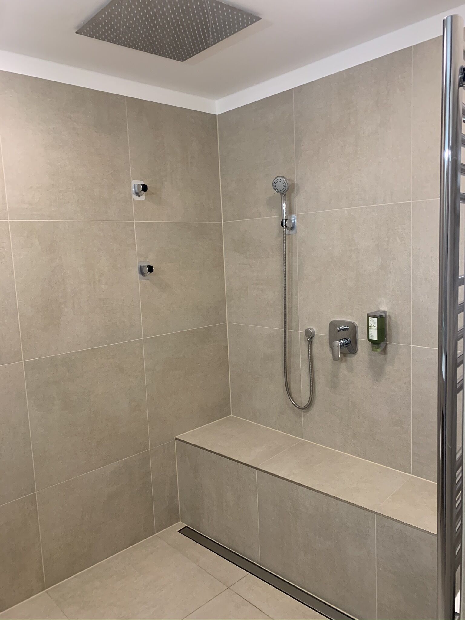 A modern shower area with a handheld showerhead, a wall-mounted control panel, and a bench.