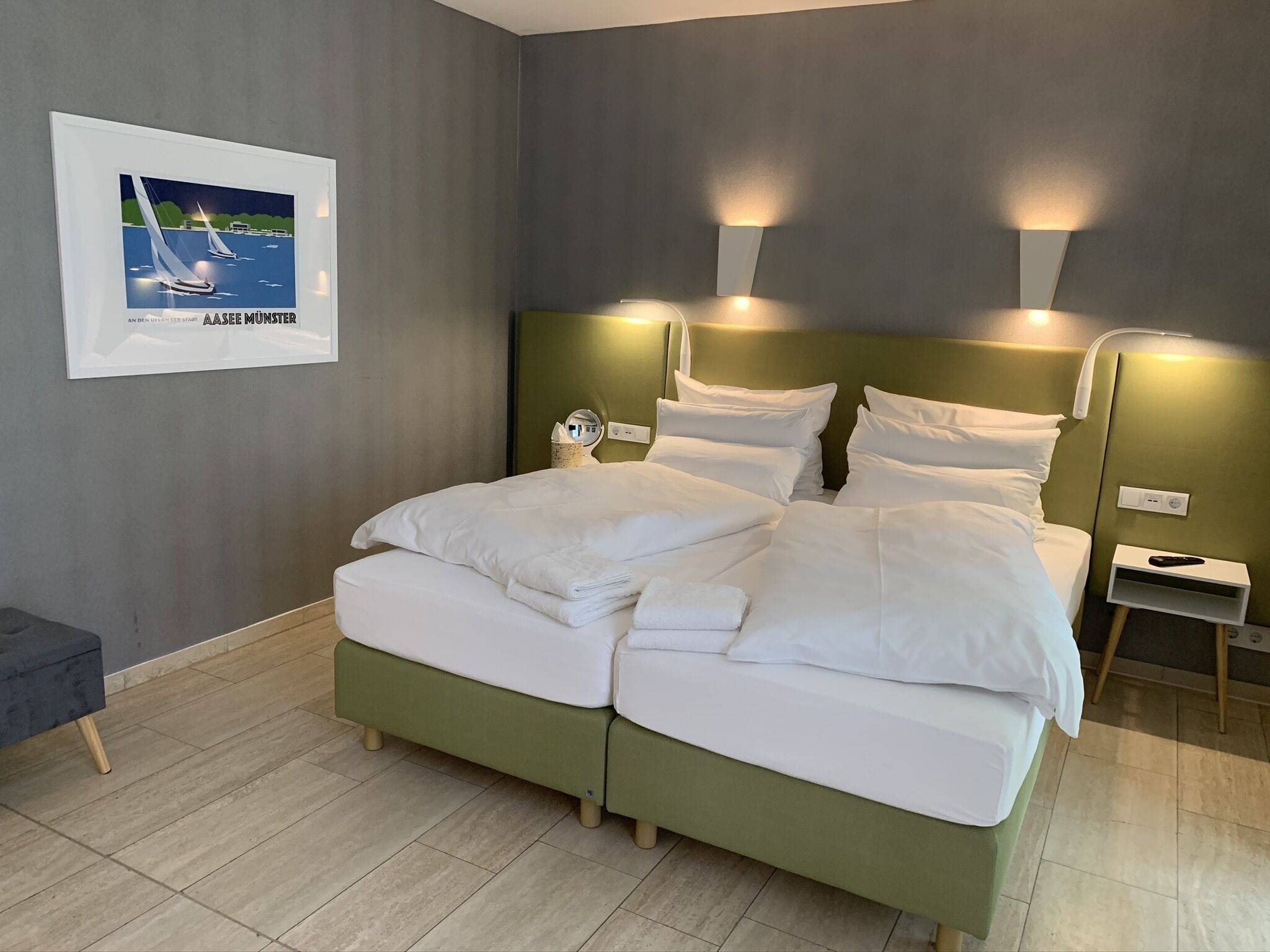 A modern hotel room with a large bed, two bedside tables, a nightstand, and a framed picture on the wall.