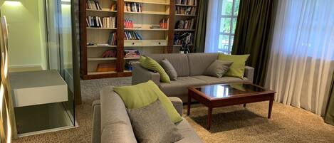 A living room with a sofa, a coffee table, and a bookshelf filled with books and a telescope.