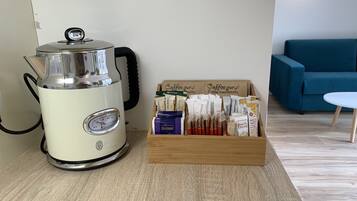 Eine Kaffeemaschine und eine Schachtel Kaffeekapseln auf einem Holztisch in einem Zimmer mit einem blauen Sofa und einem kleinen weißen Tisch.