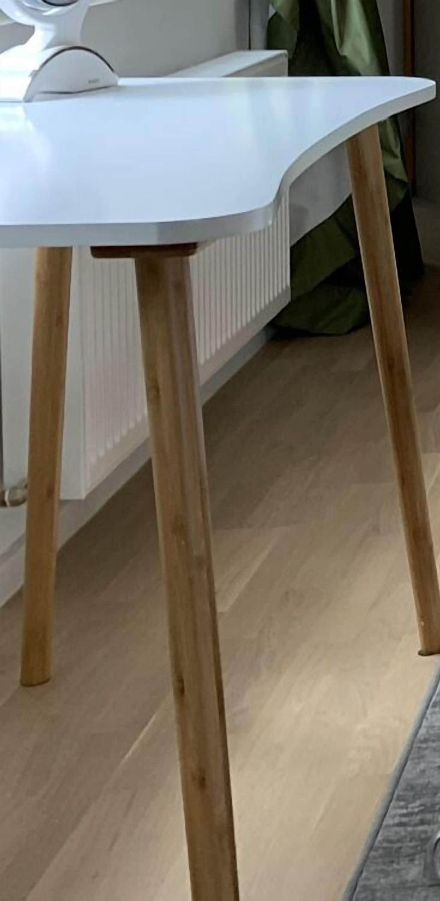 Una mesa blanca con patas de madera en una habitación con un radiador y un bolso verde en el suelo.