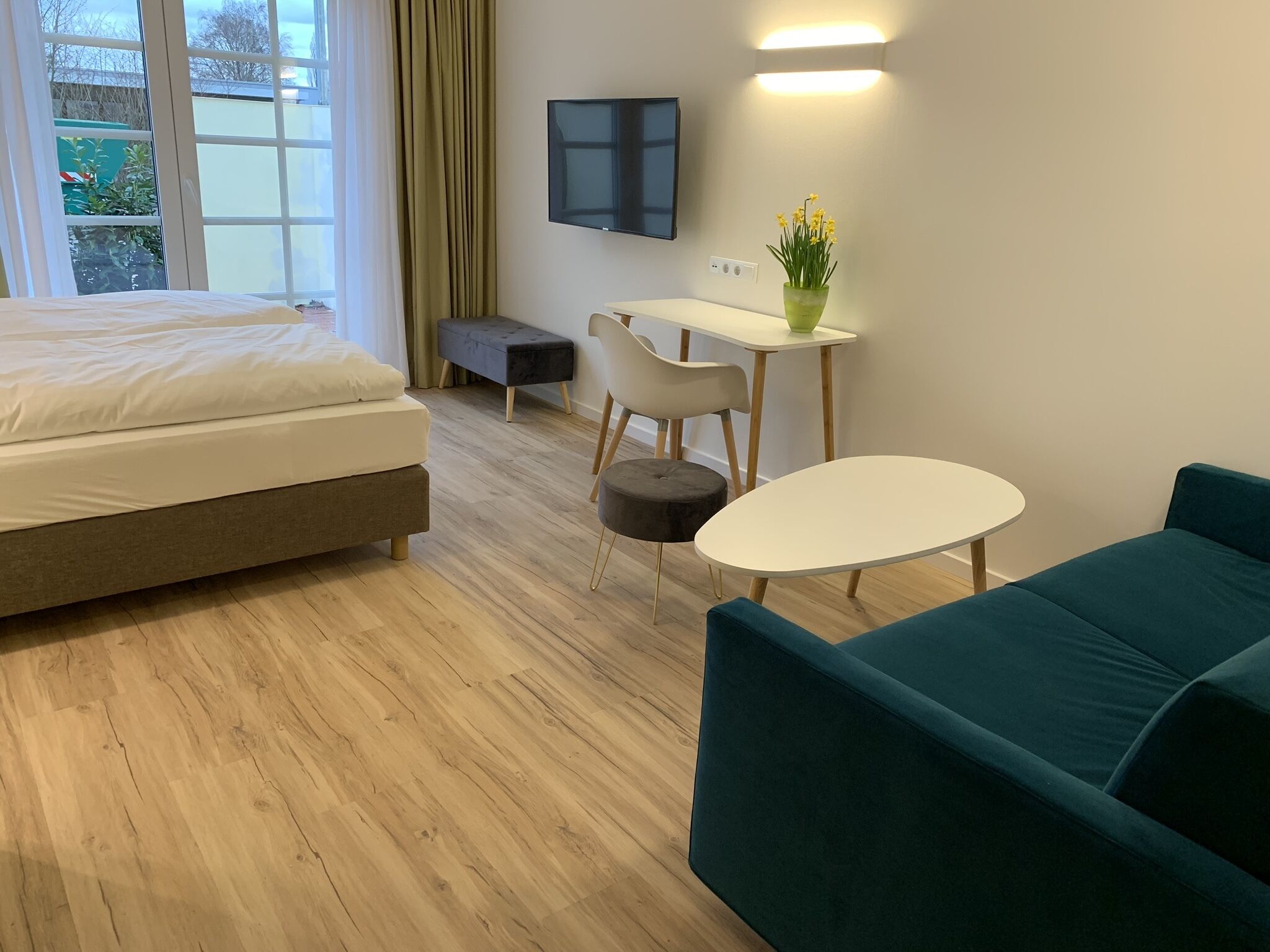 A modern hotel room with a bed, a desk, a chair, a small table, and a sofa.