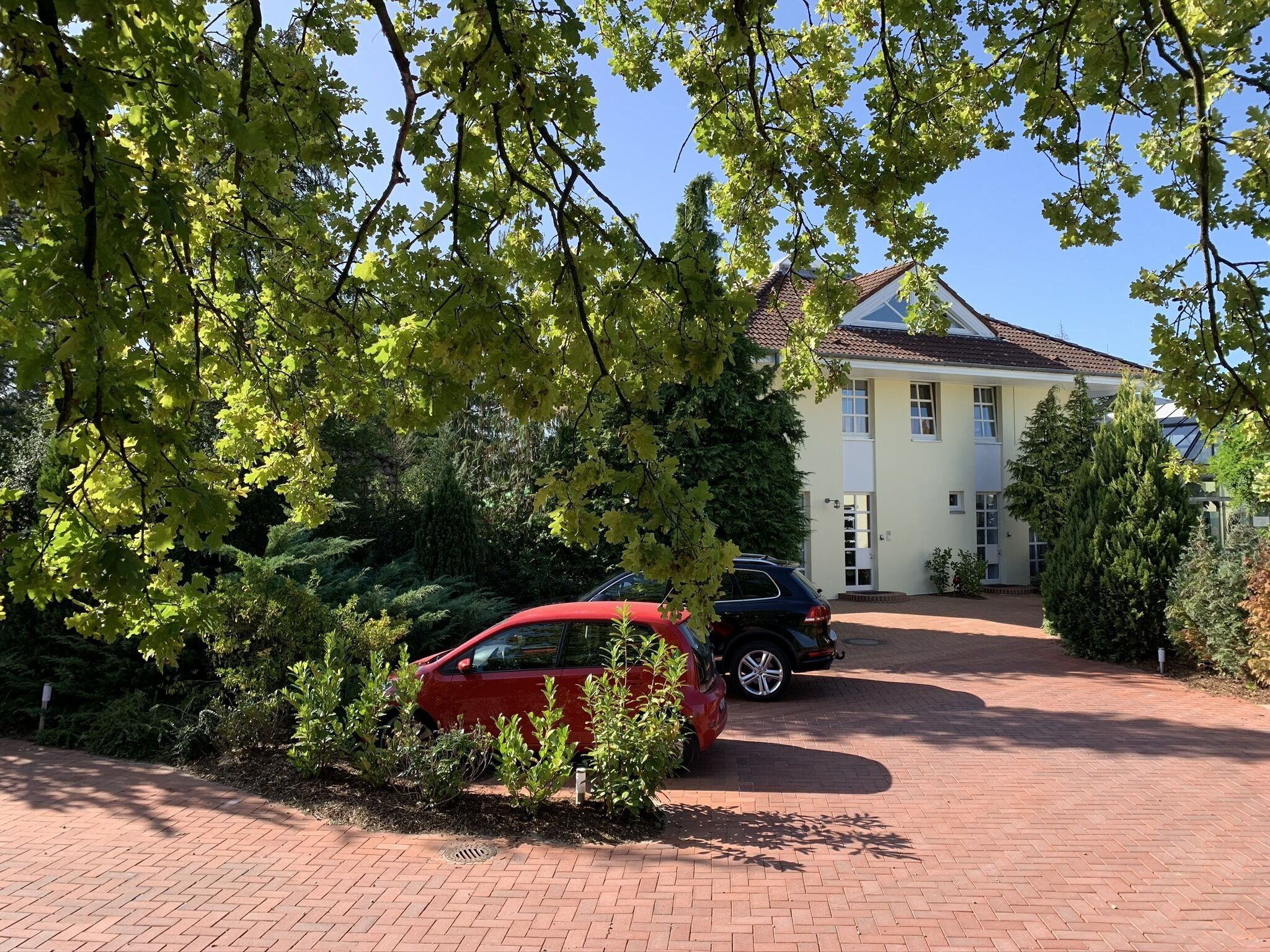 A house with a paved driveway, two cars parked, and surrounding greenery.
