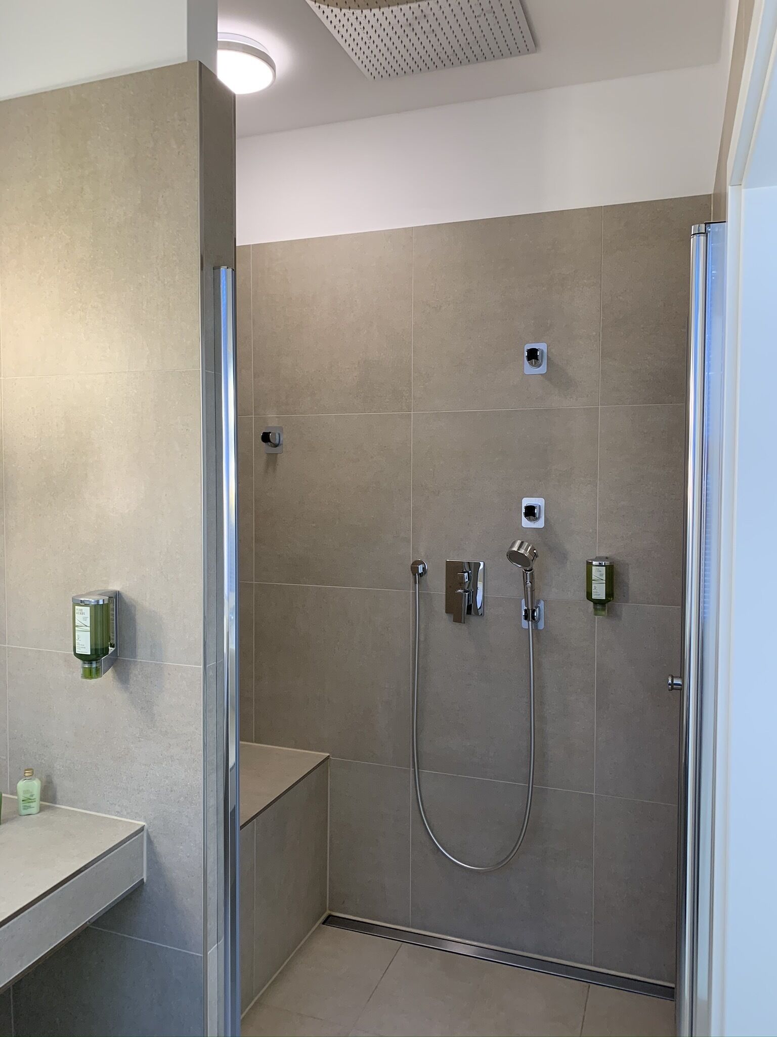 Un espace douche moderne doté d’une porte en verre, d’un banc et d’un distributeur de savon fixé au mur.