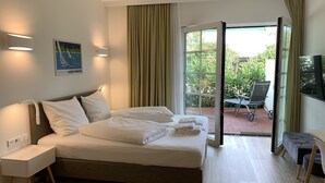 Una camera d'albergo con un letto, comodini, una TV e vista sul giardino attraverso la porta aperta.