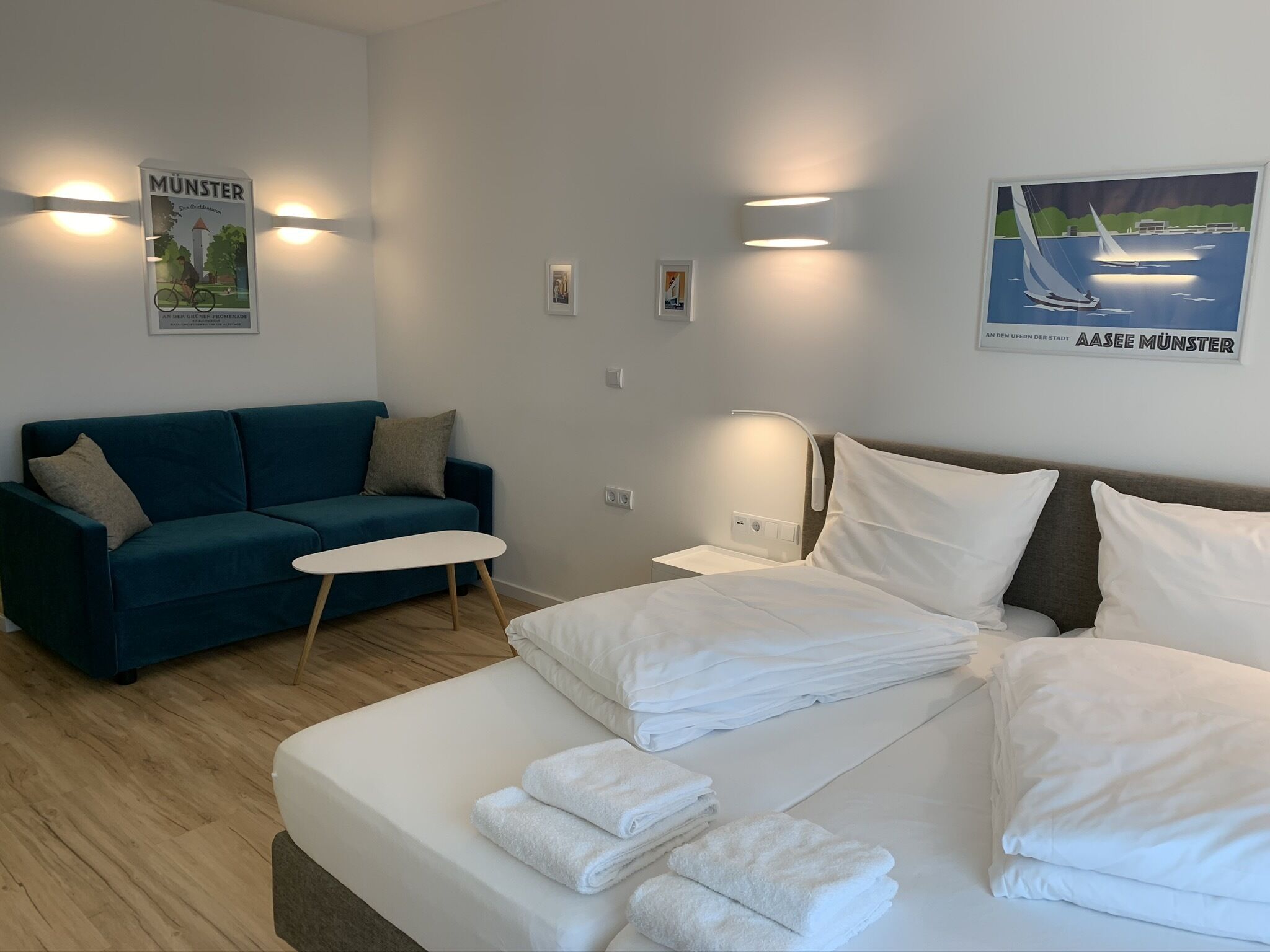 A hotel room with a bed, a blue sofa, a small table, and wall-mounted lights.