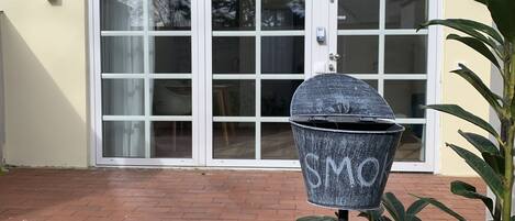 A metal trash can with the word "SMO" on it, placed in front of a house with a brick patio and a sliding glass door.