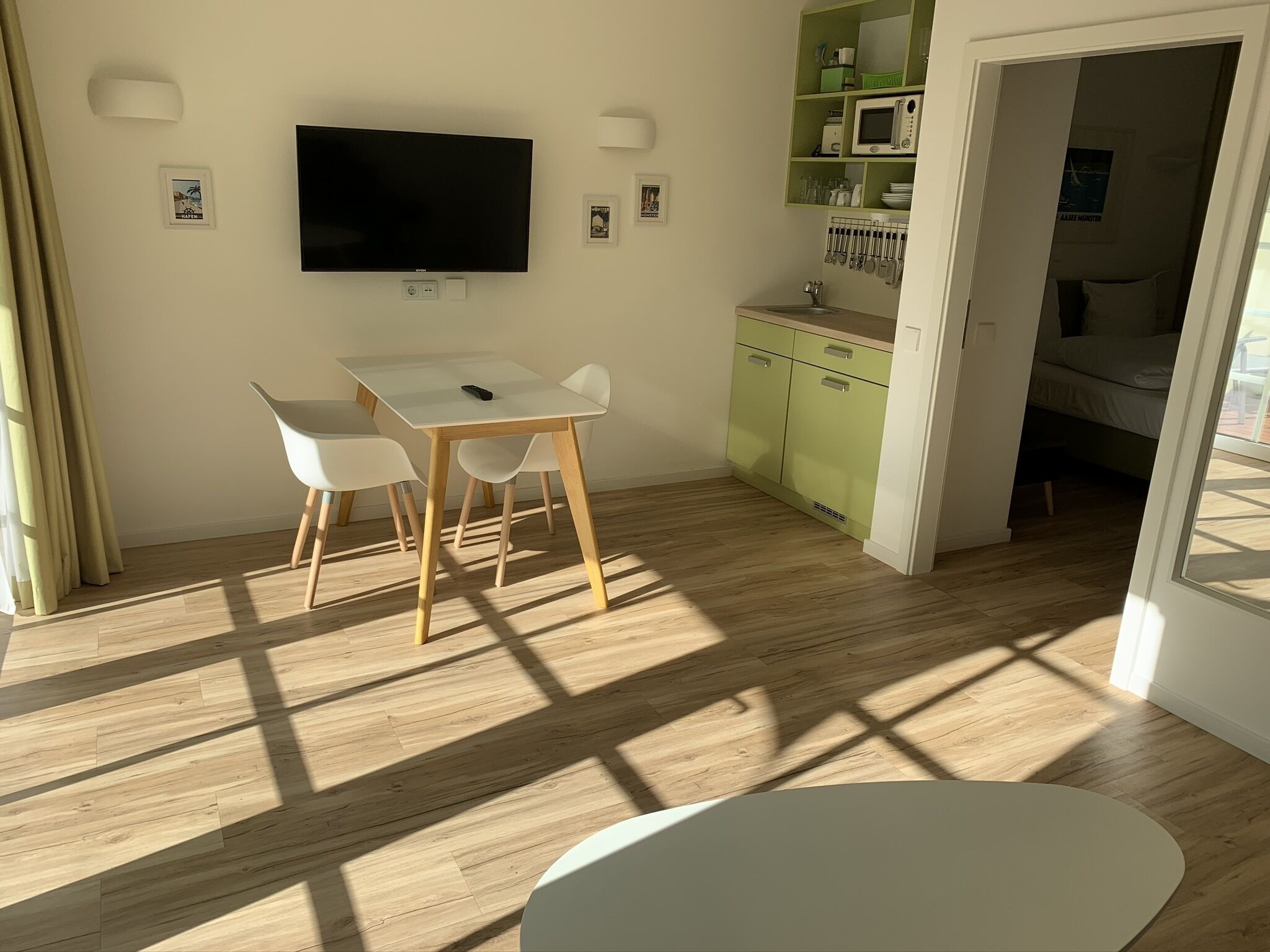 A modern room with a dining table, chairs, a flat-screen TV, a kitchen area, and a bed.