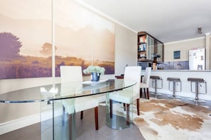 Enjoy meals at the glass-top dining table surrounded by comfortable chairs, with a bar and refrigerator nearby.