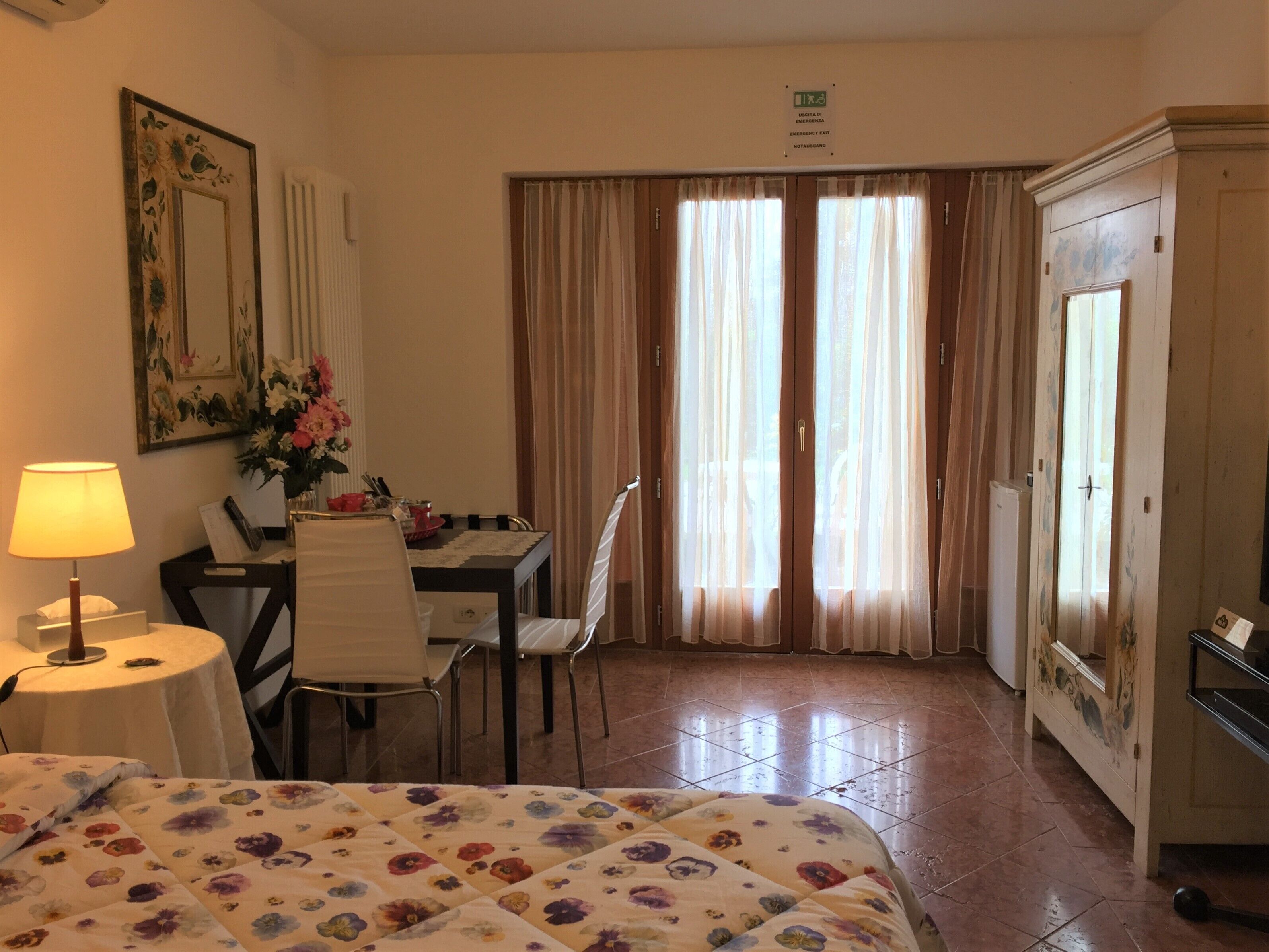 A hotel room with a bed, a desk with a chair, a lamp, a dining table with chairs, and a cabinet.