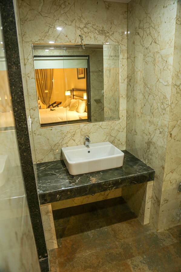 Un baño con lavamanos de mármol, un espejo y una ducha.